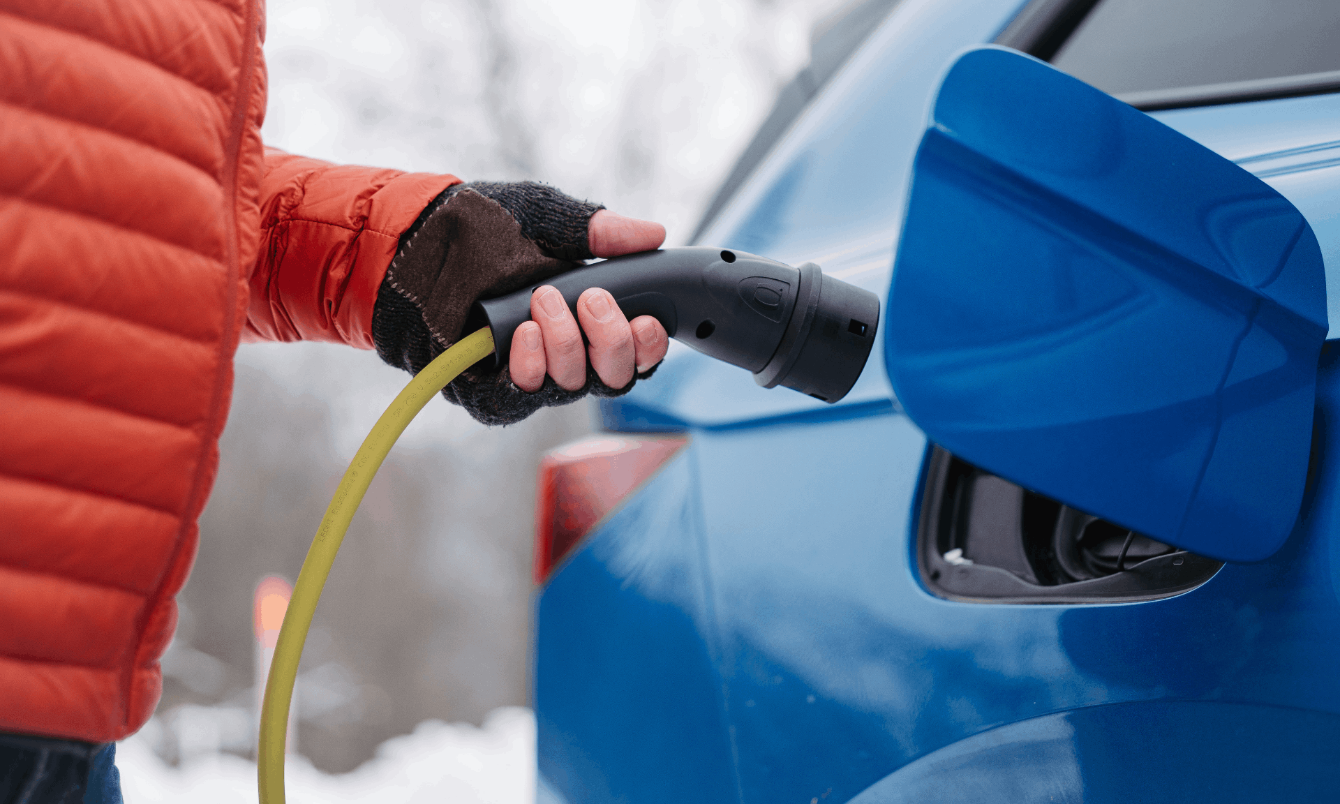 hand plugging in a blue electric car