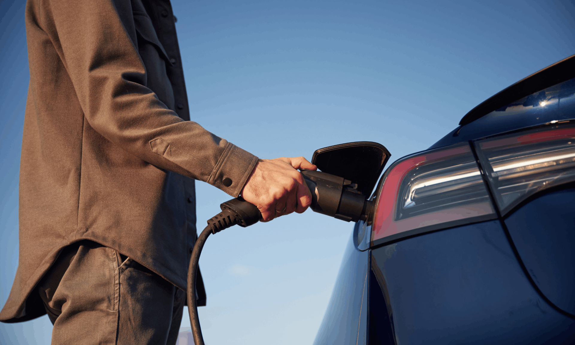 man in a shirt plugging a tesla electric vehicle in to charge