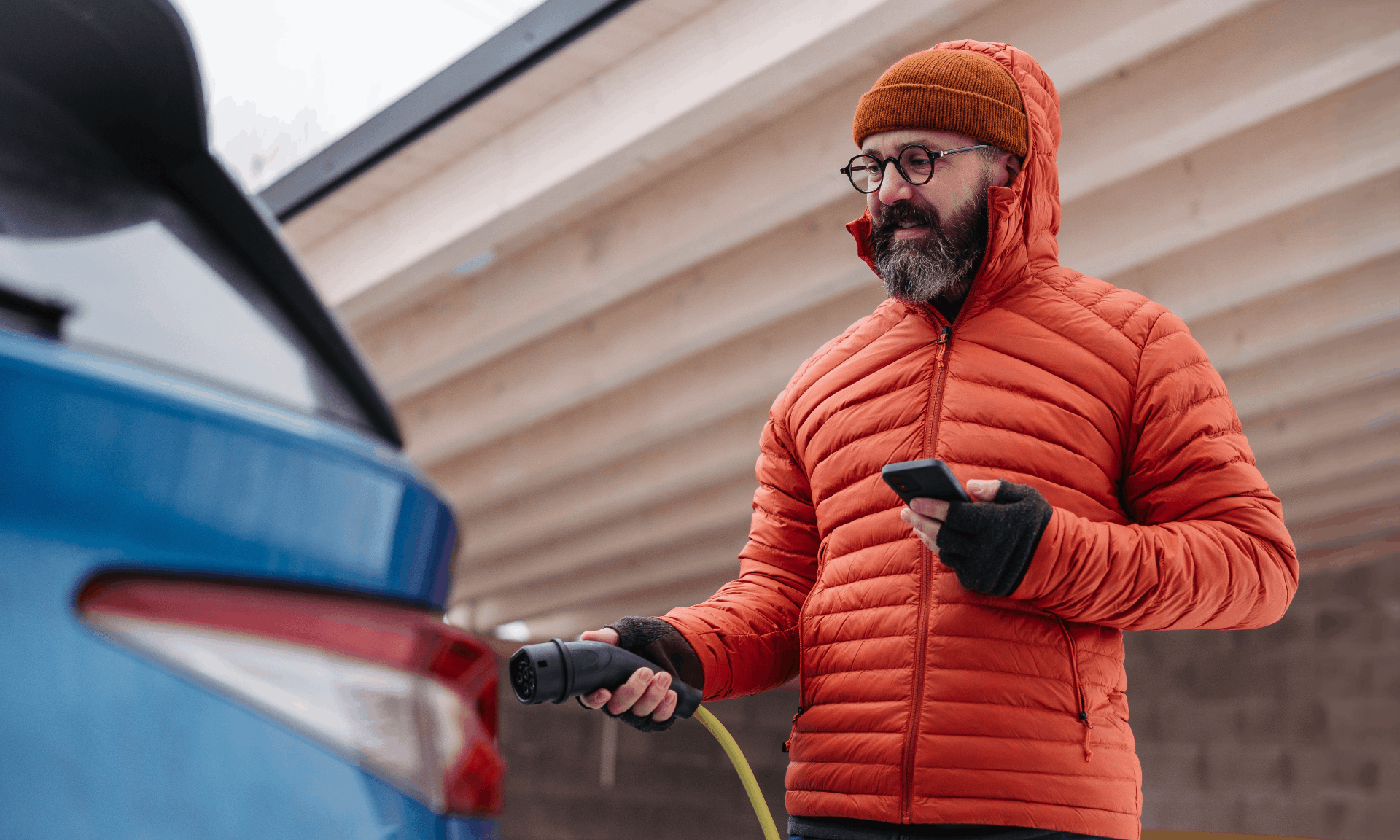 man in orange coat charging his electric car