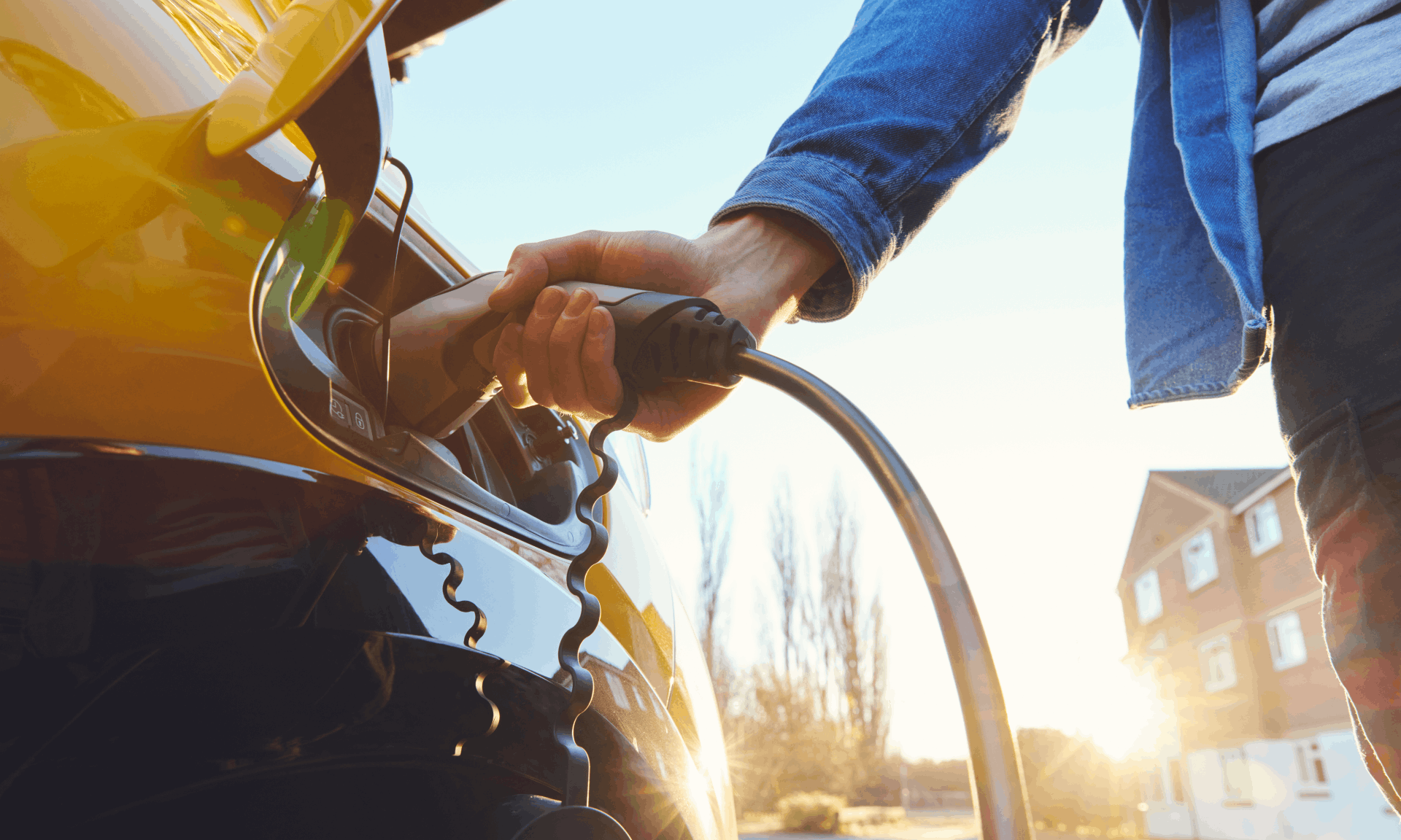 man plugging in yellow electric vehicle to charge